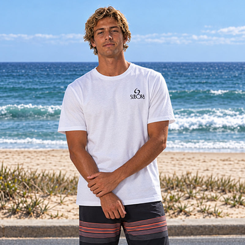 Front view of the Subora Summer Chaos Tee in White on a male model standing by the beach, showing the black Subora logo chest print