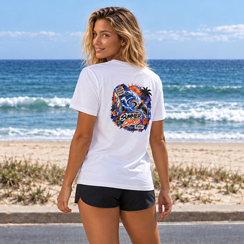 Back view of the Subora Summer Chaos Tee in White on a female model by the beach, showing the full-colour Summer Chaos street-art back print with wave, shark, palms and surfboard