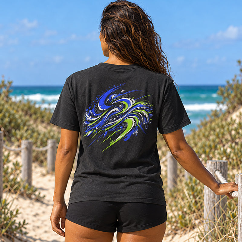 Back view of the Subora Motion Tee in Black on a female model on a beach dune track, showing the full-colour blue and lime green swirling wave back print