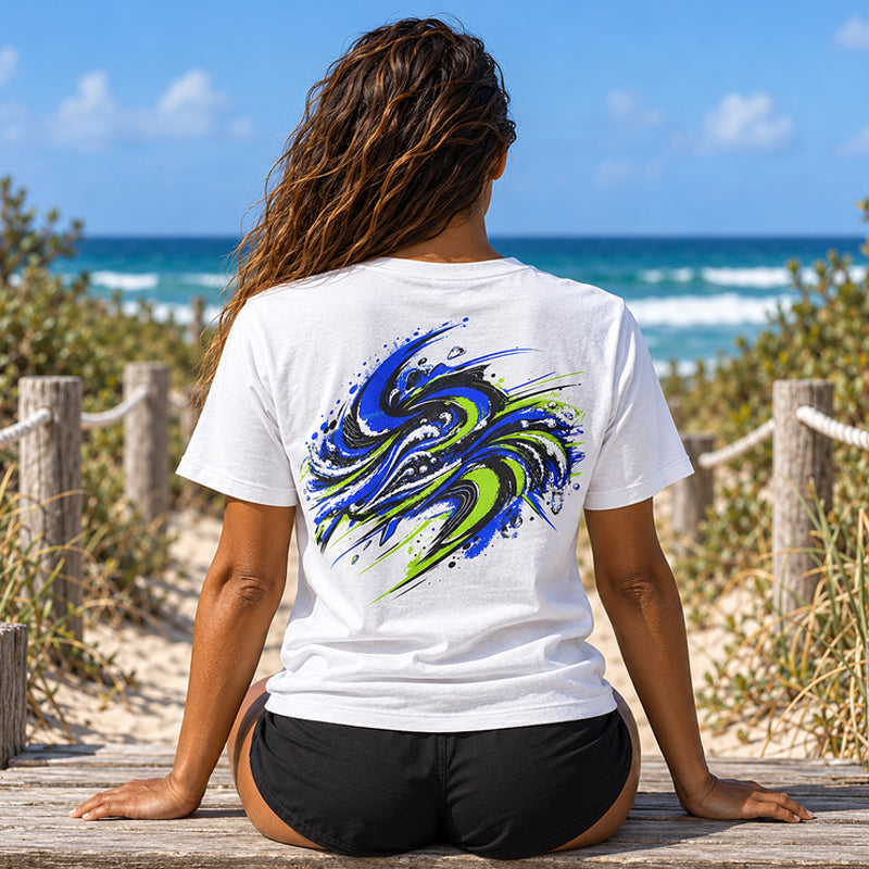 Back view of the Subora Motion Tee in White on a female model sitting on a beach boardwalk, showing the full-colour blue and lime green swirling wave back print